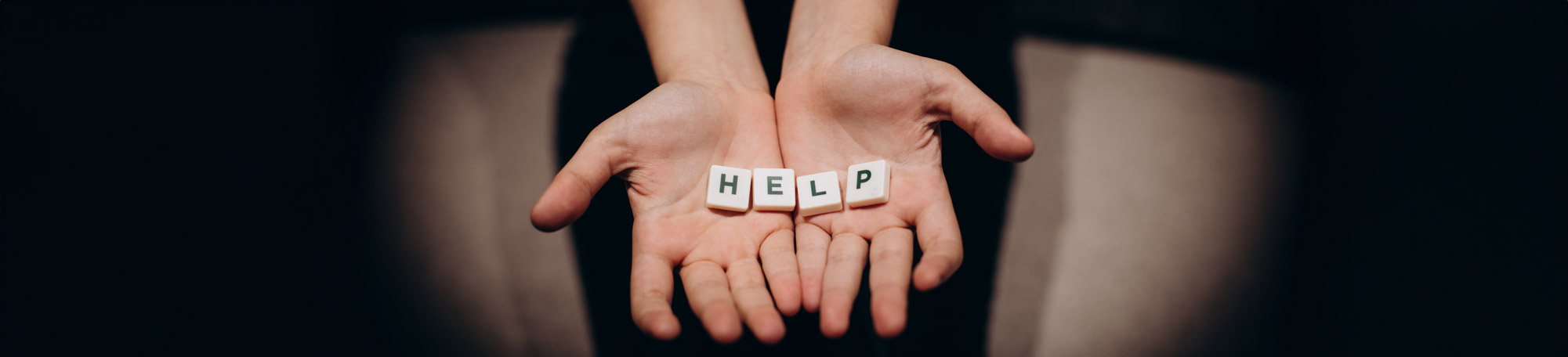 A dark image if a teenage girls hands reaching out toward you holding letters that spell out 'HELP'.