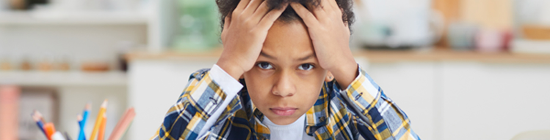 Image of a young bow in a classroom. He looks frustrated and has his head in his hands looking down