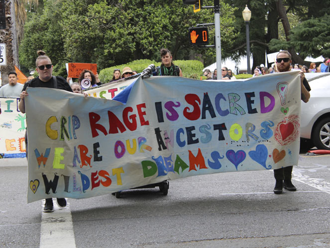 A crowd of people in a demonstration. They are crossing the street holding up a large banner.