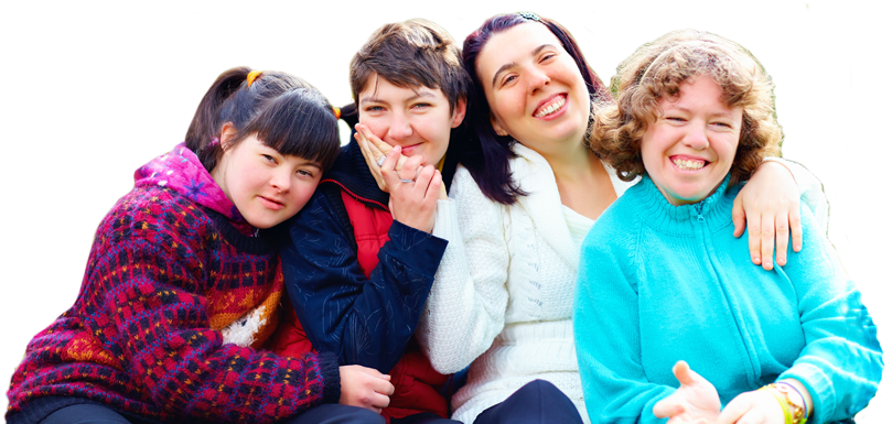 Image of four young women with a developmental disability sitting with each other closely. They are all smiling as they sit outside on a cool day.