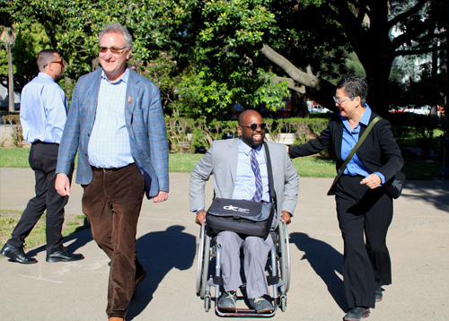 Three DRC employees walking outside the CA State Capital building. One of them is in a wheelchair.