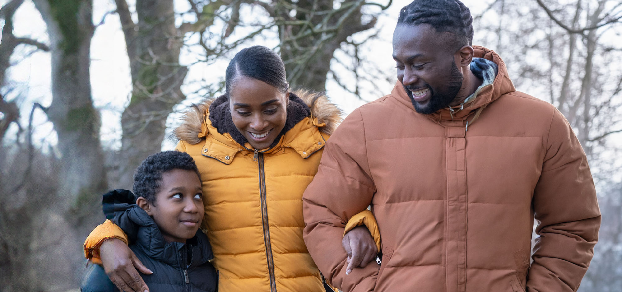 A black family with a husband and wife and their young daughter going for a walk on a cold day.