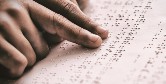 Close up photo of a man's hands reading a braille document.