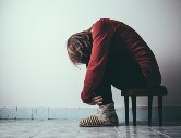 A image of a youth sitting in a chair all alone in a room. She is bending over with her head between her knees.