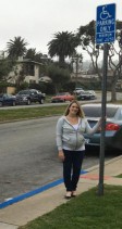 Photo of Katie Bassilios standing next to a metal pole that has a disabled parking sign on top of it.