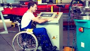 A man in a industrial plant operating machinery. He has a disablity and is in a wheel chair.