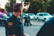 An image of a police man looking over his shoulder at two other police officers who are arresting a man.