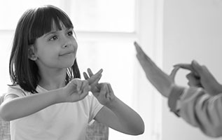 Photo of a young girl communicating in sign language to an adult.