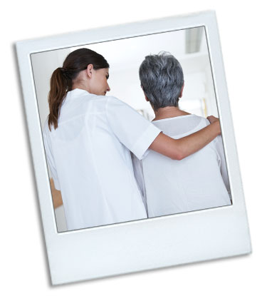 A young woman helping a elderly woman walk down a hallway. The elderly woman has a disability.