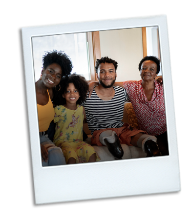 A family sitting together on a couch all smiling. The older brother in the middle has a disability.