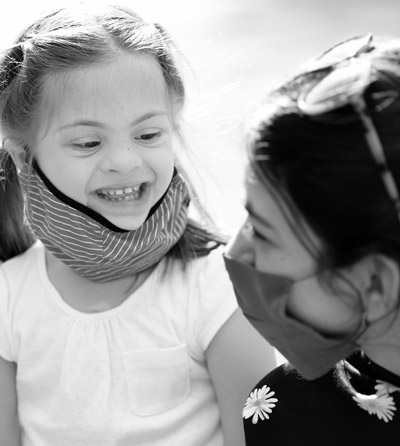 Photo of a woman hugging a young girl who has a mental disability. They both have medical masks on due to COVID-19