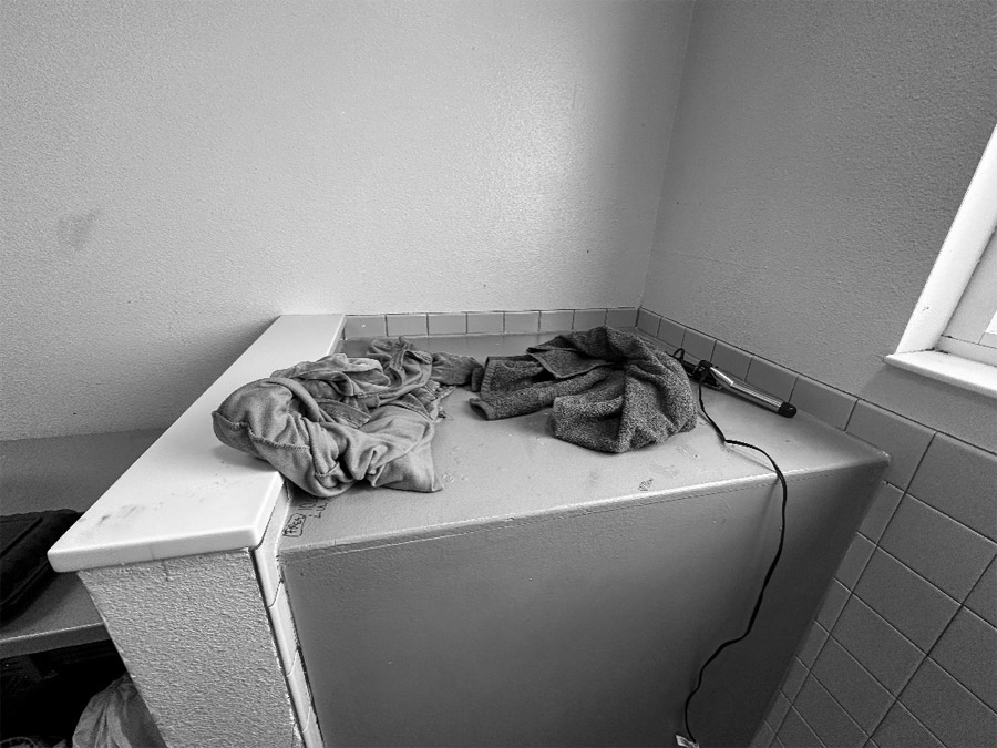 The corner of an occupied cell in the WET Center. Articles of clothing and a hair curler sit on top of a gray wooden box.