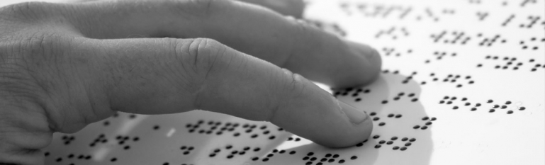 Close up of a blind person's hand reading braille on a metal sign.