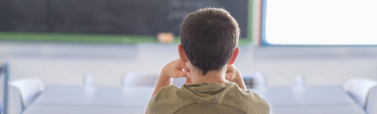 A young hispanic boy in a classroom looking at the chalkboard in front of him.