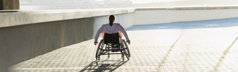 A lone person in a wheelchair struggling to go up a ramp.