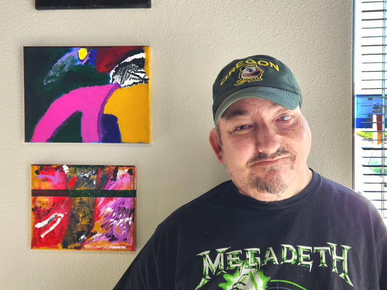 David Kossow A picture of David Kossow smiling while standing to the right of a few of his abstract paintings.