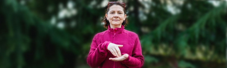 Photo of a lone deaf elderly woman. She is looking straight forward using sign language.