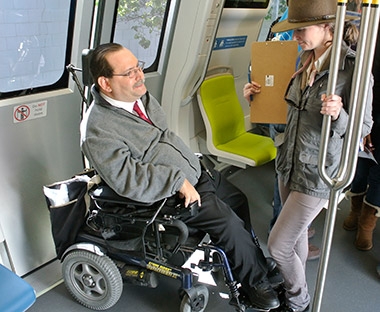 Photo of Fred Nisen in a wheelchair riding a BART train