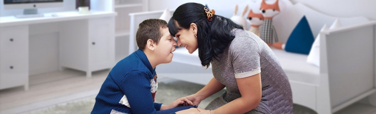 A photo of a mother with her young son who has a mental disability. They are in his room smiling together.