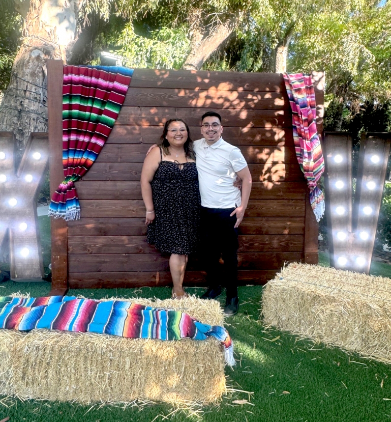 A photo of Jose and his wife in semi-formal wear and in glasses, outside in a backyard with bright festive decorations