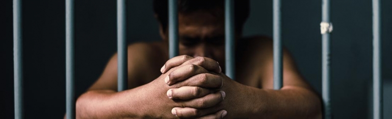 Photo of a male prisoner hanging his arms outside a jail cell.