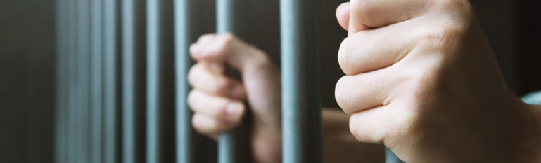 A person holding onto the bars of a jail cell.