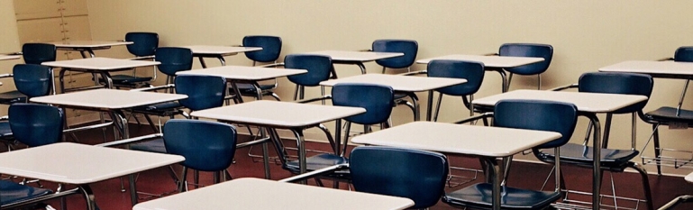 Photo of a classroom empty of children with school desks in a row. 