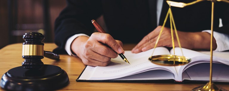 Closeup photo of a man signing a bill. A gavel and law scale are sitting on his desk.