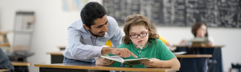 A  teacher helping a young girl with a disability with her homework.