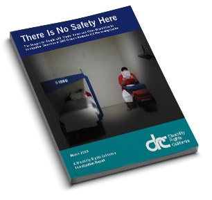 Cover of the report. I shows a image of a lone person sitting in a detention cell.