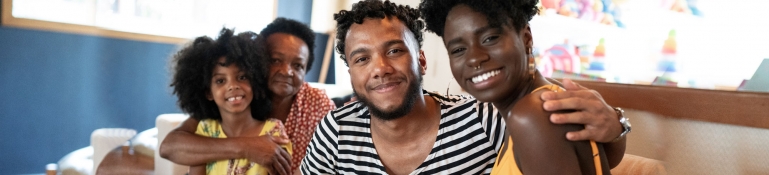 Several members of a black family sitting on a couch smiling. The young man in the center has a disability.