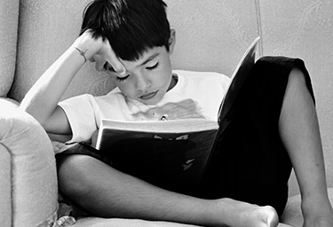 Photo of young boy struggling to read a book.
