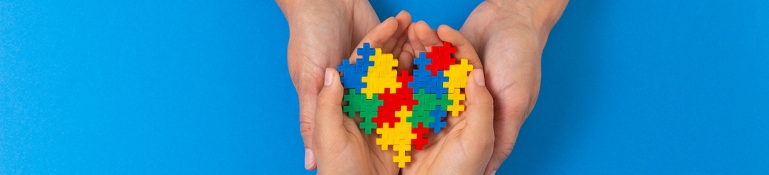 World autism awareness day concept. Female and child hands holding puzzle heart on light blue background World autism awareness day concept. Adult and kid hands holding puzzle heart on light blue background.