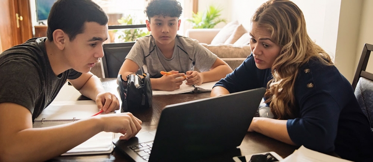 A mother helping her two children do school on their laptop