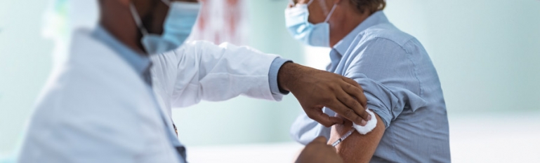 A doctor giving a elderly patient a vaccine shot in a hospital.