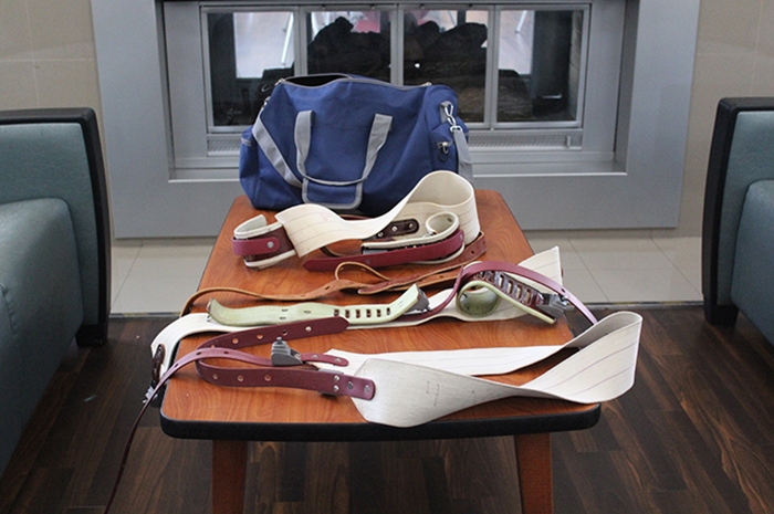 Restraint straps displayed on a table. A blue athletic duffel bag that holds the red and white leather restraint straps utilized in 5-point restraints.