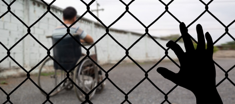 Photo of a disabled person behind a fence in a detention facility.