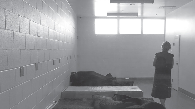 An ominous black and white photo of a person in a detention facility looking up towards a bright window.