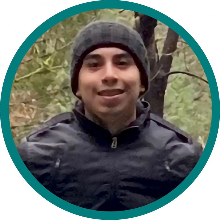 A portrait of Jose outdoors in a nature park in a beanie and a dark puffer jacket.