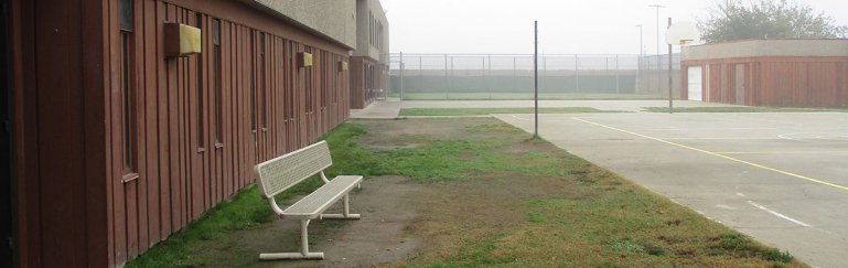 The exterior of the detention center showing a empty bench in the outside courtyard