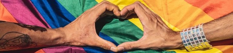 Gay couple showing heart shape with hands on rainbow flag LGBTQI Pride Event.