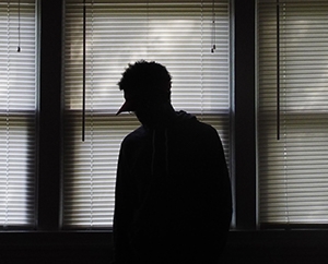 Silhouette of a man in front of windows looking down in a dark room.