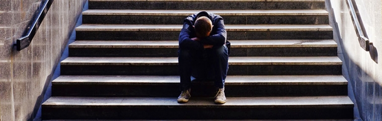 Photo of a lone student sitting at the bottom of school steps. He seems troubled and has his head between his legs.