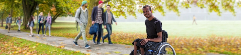 A young man on a college campus. He has a disability and is in a wheel chair.