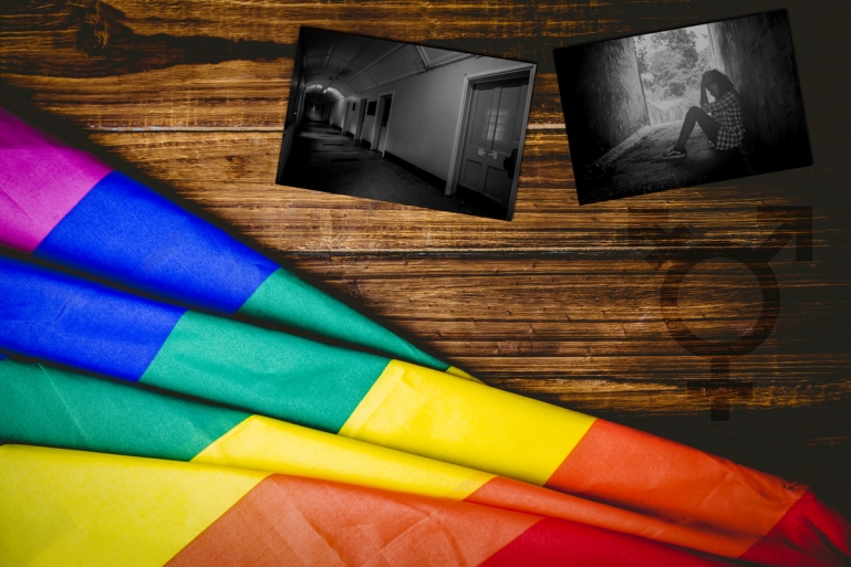 Photo of a Pride flag and two photographs laid on top of a wooden table. Photographs show a dark corridor to a detention facility and a person looking distraught.