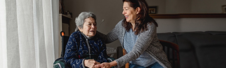 An older hispanic woman in a wheelchair being taken care at home by her adult daughter.