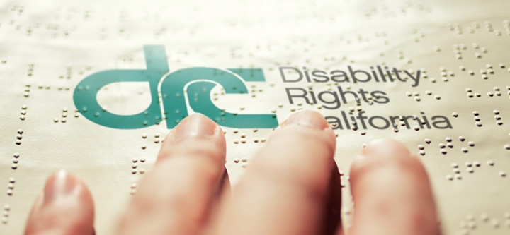 Close-up photo of a woman's fingers reading a braille document with the DRC logo printed on it.