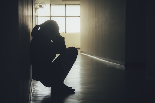 Silhouette photo of a distressed looking woman crouching in a dark hallway.