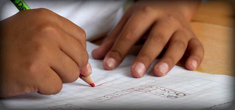 Photo of a close up of a little girls hands. She is solving a math problem on a piece of paper.