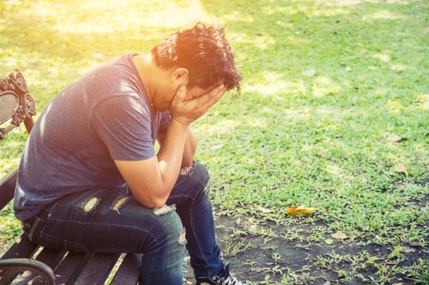 Photo of distressed looking person sitting on a bench with his face in his hands.